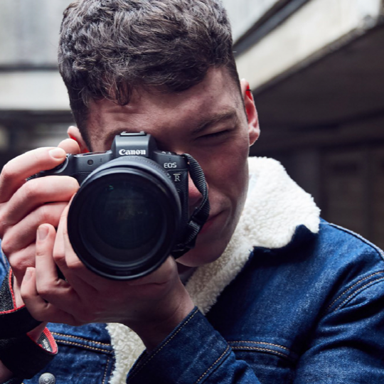 Man holding a Canon SLR Camera pointed at us 