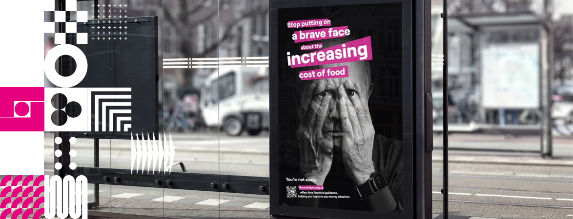 Bus Stop with a poster that has a picture of a man with hands over his eyes in black and white. The text on the poster says 'Stop putting a brave face about incrasing cost of food' To the left of hte image a mix of white and pink squares with DRPG branding