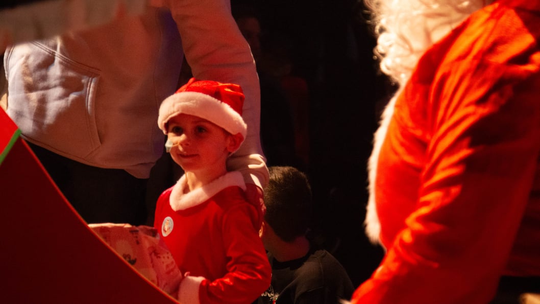 Small child holds Christmas present dressed in Christmas outfit.