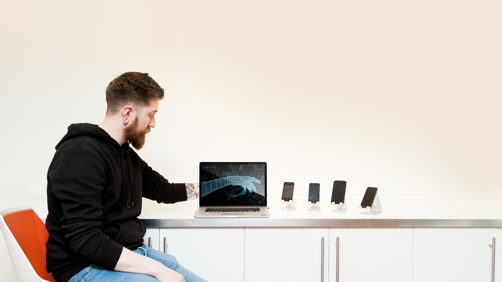 Male employee sat on orange chair with his hand merging into skeleton on laptop screen - human to technology coming together. 